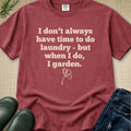 A maroon short-sleeve graphic T-shirt laid flat on a textured beige surface, with the phrase 'I don't always have time to do laundry - but when I do, I garden.' printed in light beige text and a small clover graphic below.