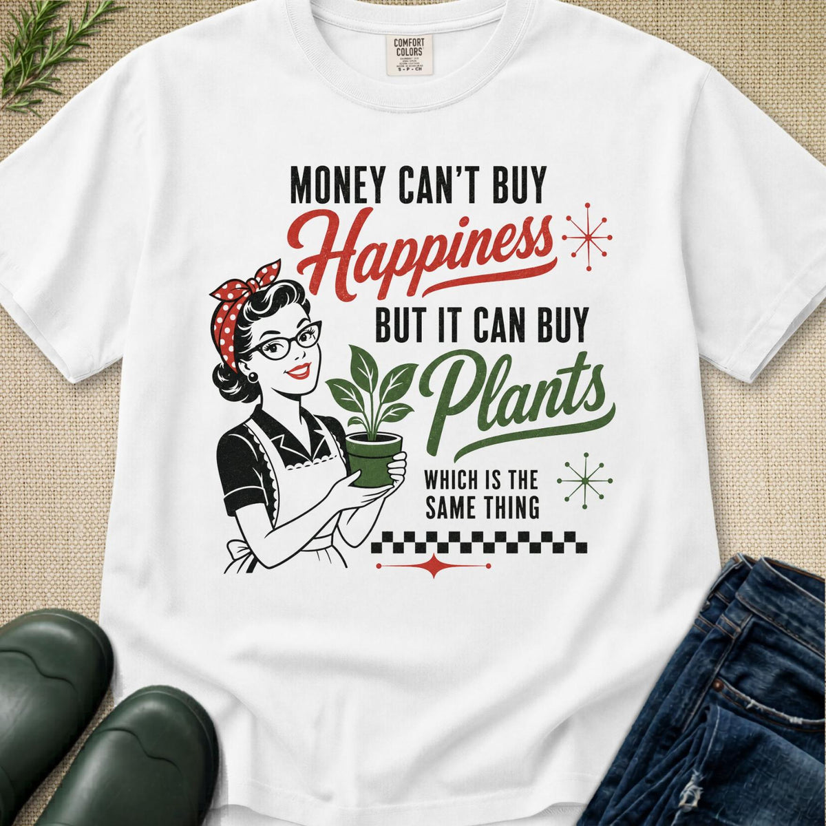 A white short-sleeve graphic T-shirt laid flat on a beige textured surface, with black, red, and green printed text and an illustration of a retro woman holding a potted plant. Jeans and dark green shoes are partially visible around the shirt as styling props.