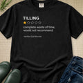A black graphic t-shirt laid flat on a textured beige fabric background, styled with dark green rain boots and blue jeans. The t-shirt features a white text graphic that reads 'TILLING' with a one-star review graphic and the quote 'complete waste of time, would not recommend -Verified Soil Microbe'.