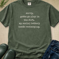 An olive green graphic t-shirt with white text that reads 'sorry, gotta go play in the dirt. my social battery needs recharging.