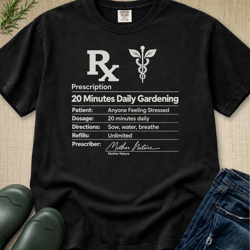 A black graphic t-shirt laid flat on a textured beige fabric background, styled with green leaves, dark green rain boots, and blue jeans. The t-shirt features a white printed graphic resembling a prescription form with the text 'Prescription 20 Minutes Daily Gardening' and a caduceus symbol.